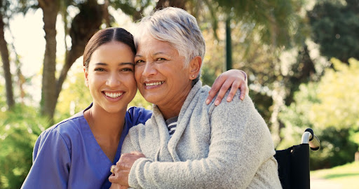 A female nurse hugs a senior woman in a wheelchair outdoors in her garden